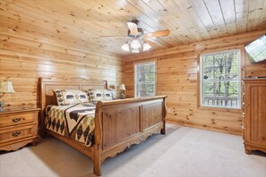 Dormitorio de cabaña de madera con cama, cómoda y ventilador de techo.