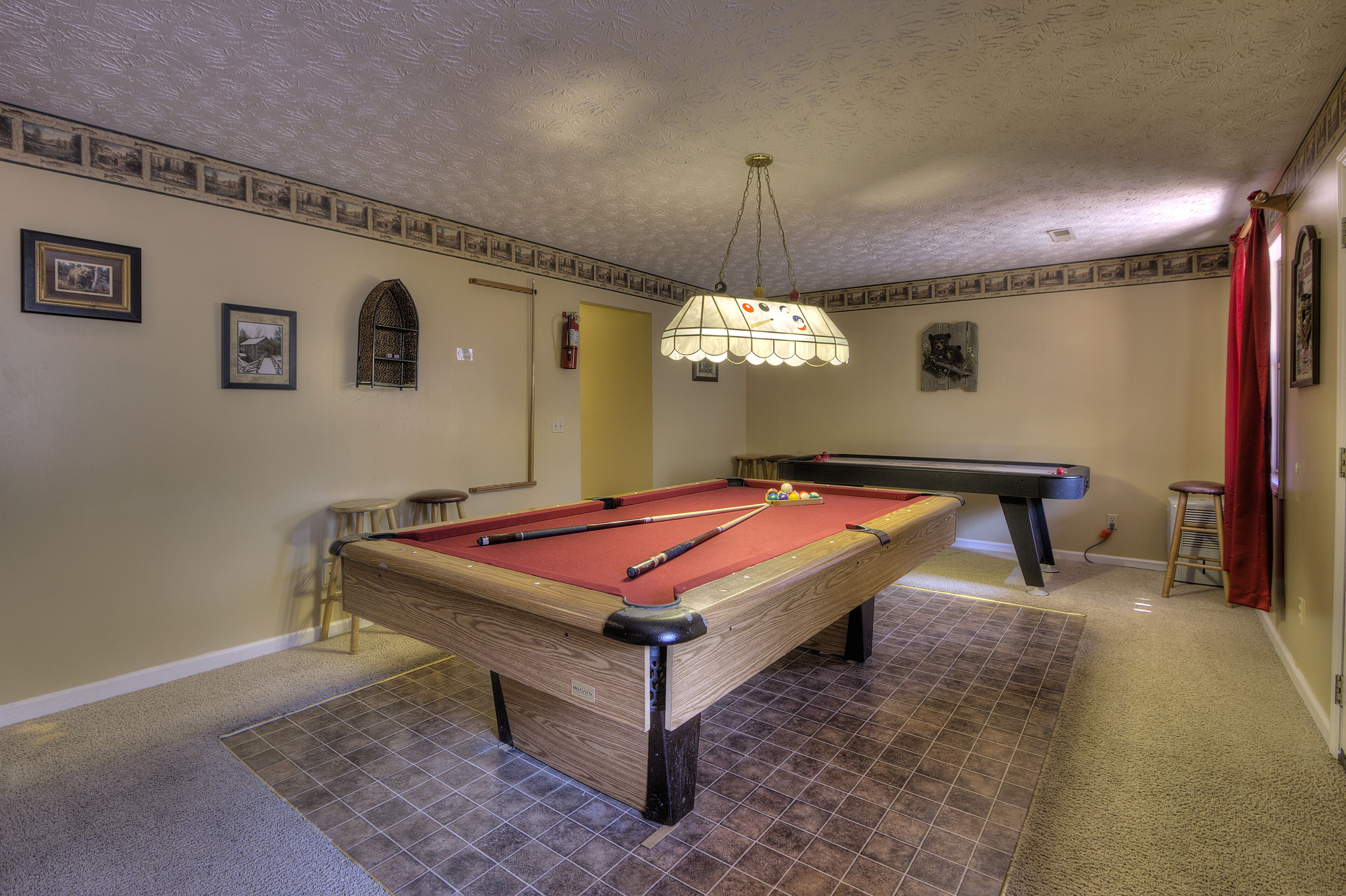 A pool table in a room with a patterned ceiling and walls, a small stool, and a red curtain.