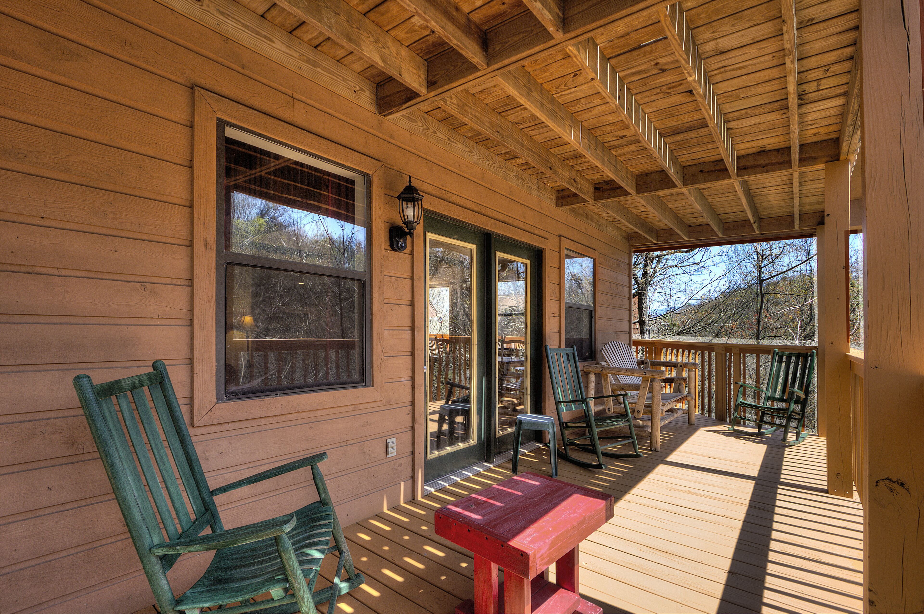 A wooden deck with chairs and a table, a covered porch, and large windows.