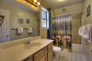 A bathroom with a large mirror, a bathtub, a toilet, and a shower curtain with a forest scene. - Bear Run Getaway #1136 (Gatlinburg)