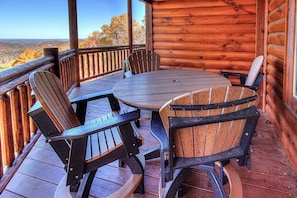 A wooden deck with a round table and four Adirondack chairs.
