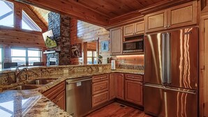 A modern kitchen with granite countertops, stainless steel appliances, wooden cabinets, and a stone fireplace. - Majestic View Lodge #426 (Sevierville)