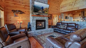 A cozy cabin interior with a stone fireplace, leather recliners, a flat-screen TV, and a kitchen area. - Majestic View Lodge #426 (Sevierville)