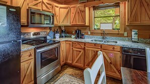 Una cocina con armarios de madera, electrodomésticos de acero inoxidable, un microondas y un ventanal con vistas a árboles.