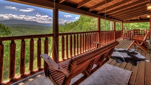 Una terraza de madera con un banco y sillas, con vistas a un paisaje montañoso.