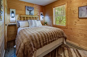 A wooden-paneled bedroom with a bed, two bedside tables, a window with blinds, and a wall-mounted light fixture.