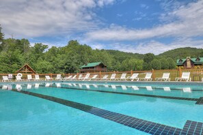 A swimming pool with clear blue water, surrounded by wooden deck chairs and a wooden fence.
