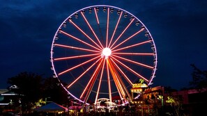 A large Ferris wheel with red and white lights, surrounded by buildings and trees.