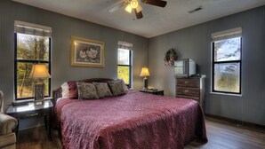 A bedroom with a large bed, two bedside lamps, a ceiling fan, a dresser, and a television on a dresser. - Kickback Shack #298 (Sevierville)