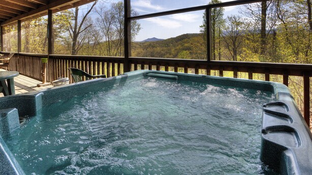 A hot tub with a wooden deck and a view of a forested mountain range. - Kickback Shack #298 (Sevierville)