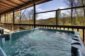 Een hottub met een houten terras en uitzicht op een bebost berglandschap.