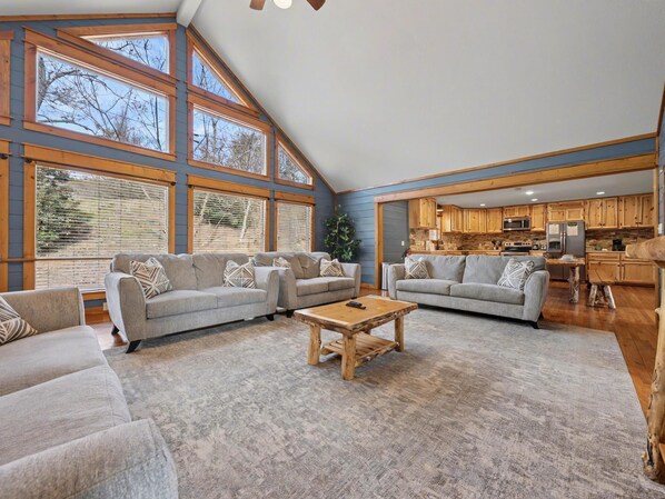 A spacious living room with large windows, a kitchen, and a dining area.
