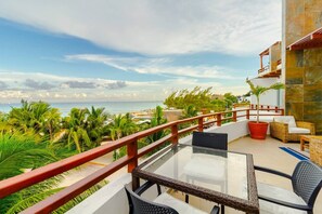 A balcony with a glass table and chairs, overlooking a beach with palm trees and a view of the ocean. - Beachfront Penthouse! Private Jacuzzi! Live the Dream! (Playa del Carmen)