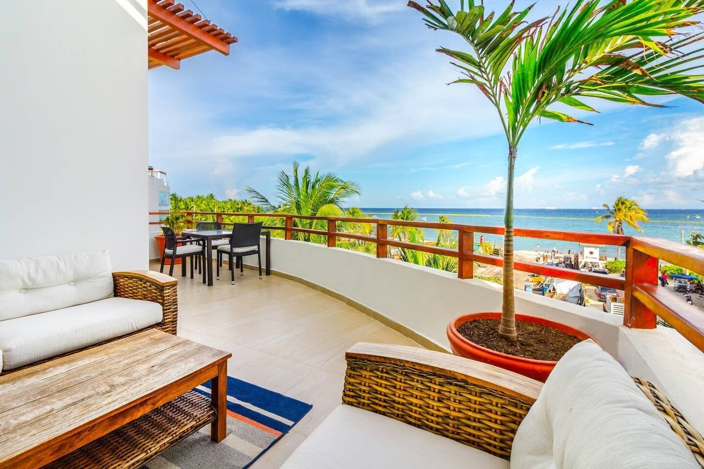 Uma varanda com vista para a praia, móveis de vime e um vaso de planta.