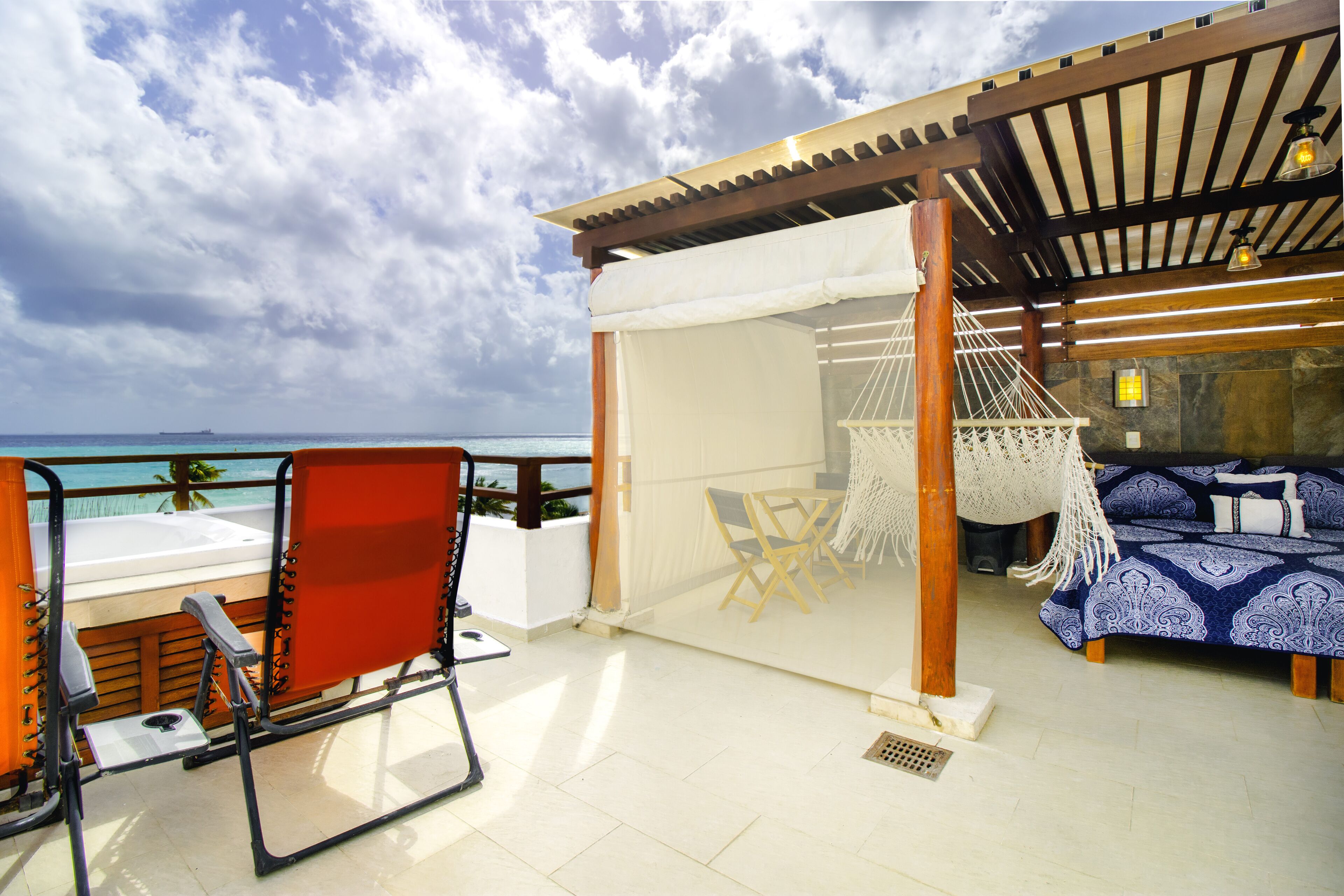A balcony with a view of the ocean, a hammock, a bed, and a table with chairs.