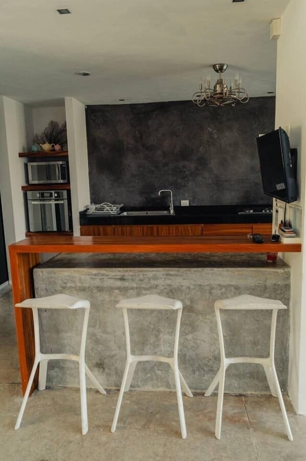 A modern kitchen with a dark backsplash, a wooden countertop, and a built-in sink. There are three white bar stools in front of the counter. - Breathtaking Beach Villa, Feel the Inviting Vibe! (Progreso)