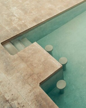 Una piscina con agua cristalina, rodeada de baldosas color crema.