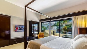 Una habitación de hotel moderna con una cama grande, un televisor montado en la pared, un balcón con plantas y vistas al exterior.