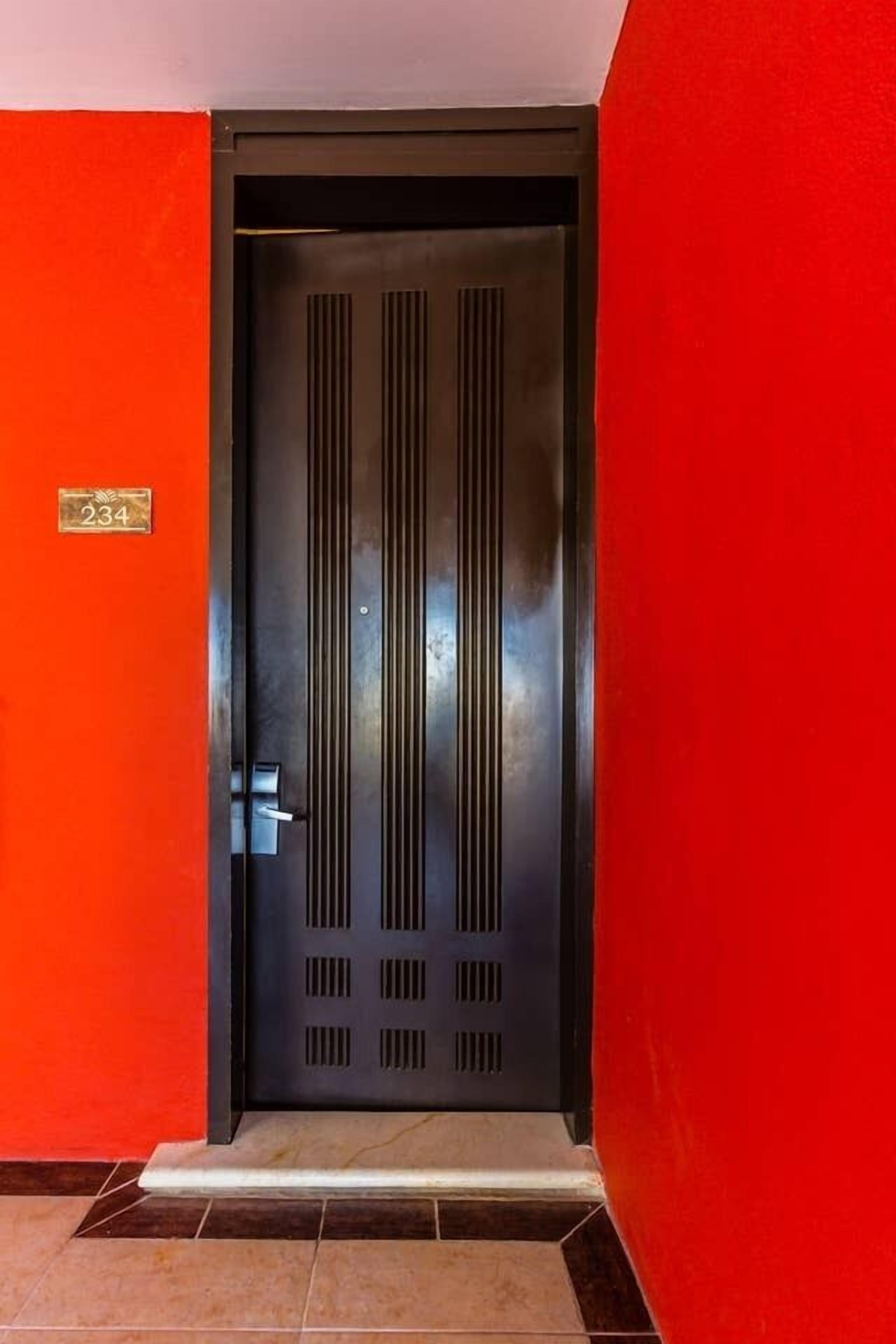 A black door with a number plate, set in a red wall with a tiled floor.