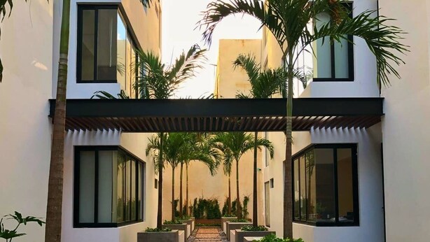 A modern building with a central pathway flanked by planters and palm trees. - 3-br Condo, Partial Ocean View, 2blocks From Ocean (Playa del Carmen)
