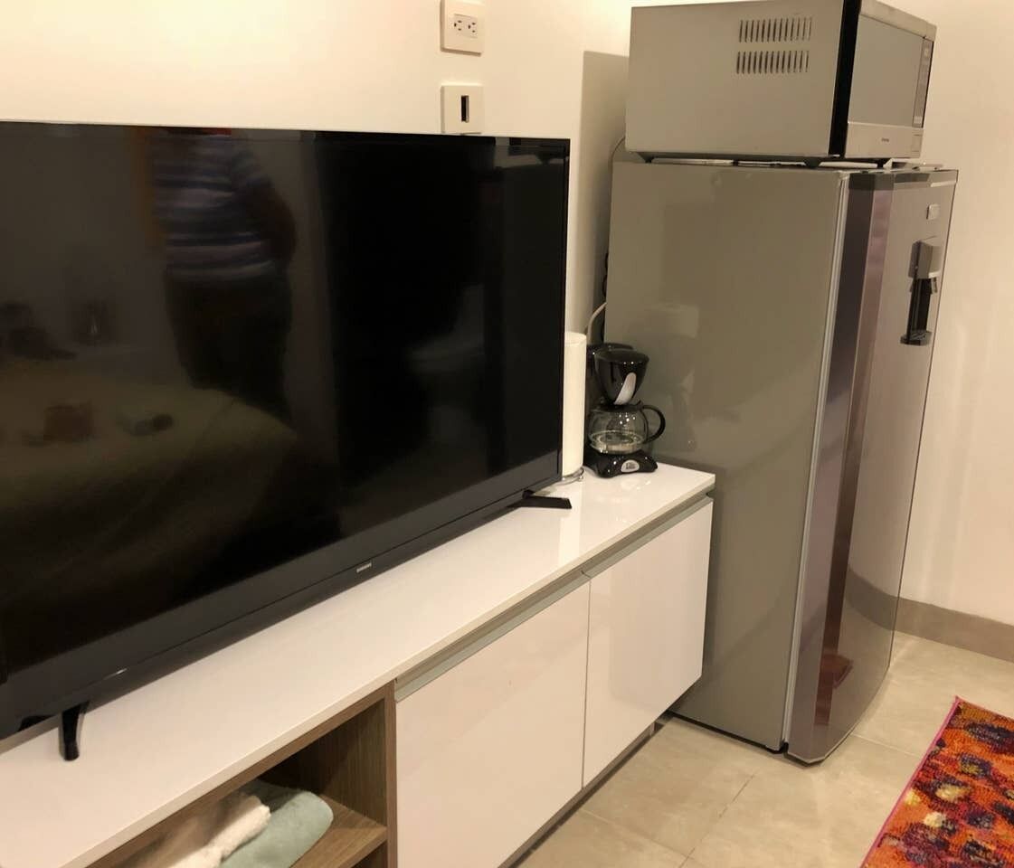 A kitchenette with a large flat-screen TV, a coffee maker, and a refrigerator.
