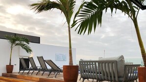 A rooftop lounge area with wooden steps, lounge chairs, and potted palm trees. - 3-br Condo, Partial Ocean View, 2blocks From Ocean (Playa del Carmen)