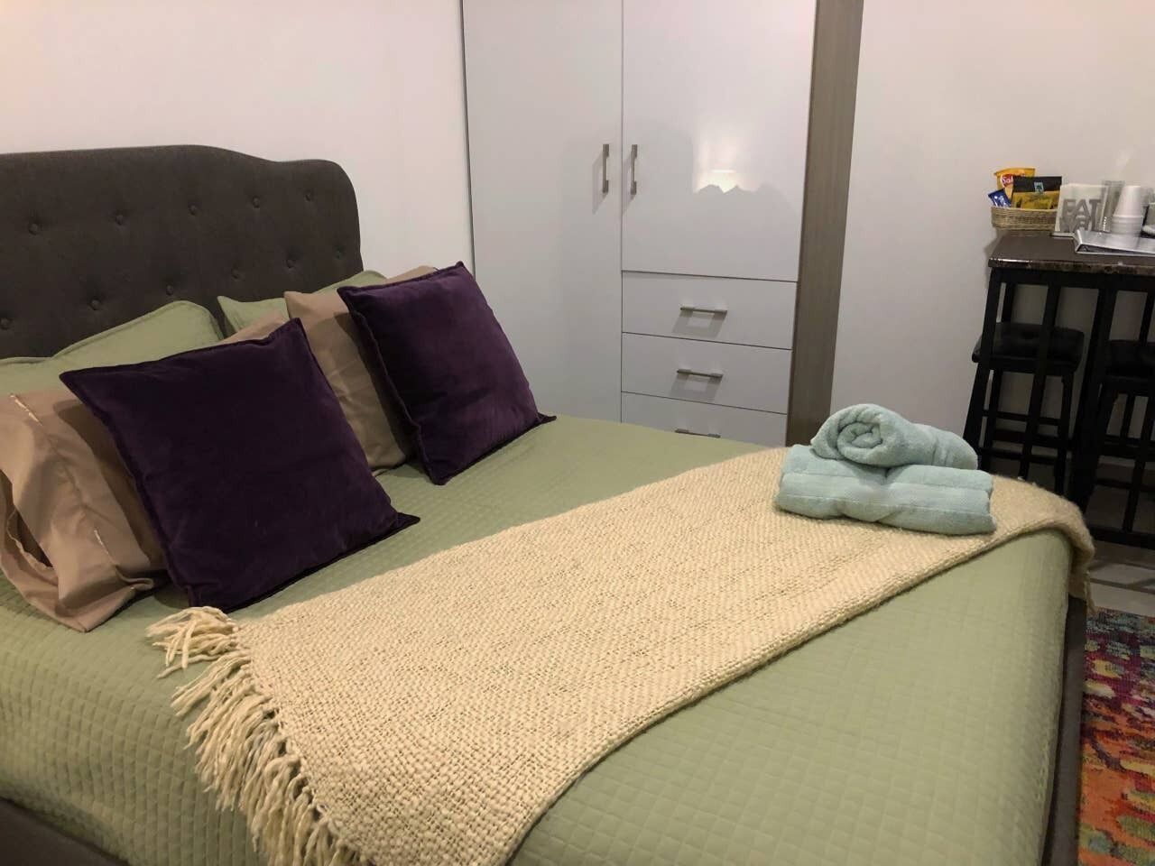 A neatly made bed with a green bedspread, a beige throw blanket, and several pillows.