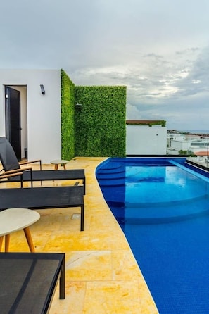 A rooftop pool area with a curved pool, a seating area with a table and chairs, and a green hedge wall. - Brand New Studio! Steps From The Beach! AC! Best! (Playa del Carmen)