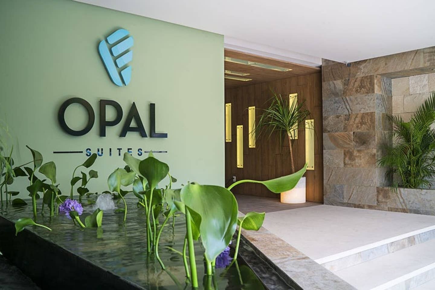 A reception area with a sign for OPAL SUITES, a water feature with plants, and a stone wall.