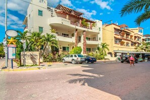 A multi-story building with balconies, a street with parked cars, and a pedestrian. - Dream Location! 2BR Near Beach+clubs!! Sleeps 6!! (Playa del Carmen)