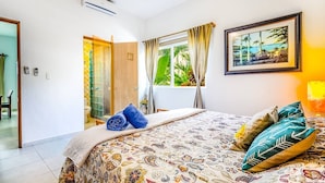 A hotel room with a bed, a window with curtains, a painting, and a bathroom with a glass door. - Dream Location! 2BR Near Beach+clubs!! Sleeps 6!! (Playa del Carmen)