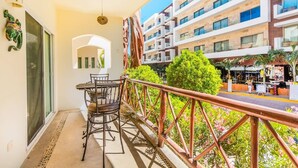 A balcony with a table and chairs, overlooking a building with multiple floors and balconies. - Dream Location! 2BR Near Beach+clubs!! Sleeps 6!! (Playa del Carmen)