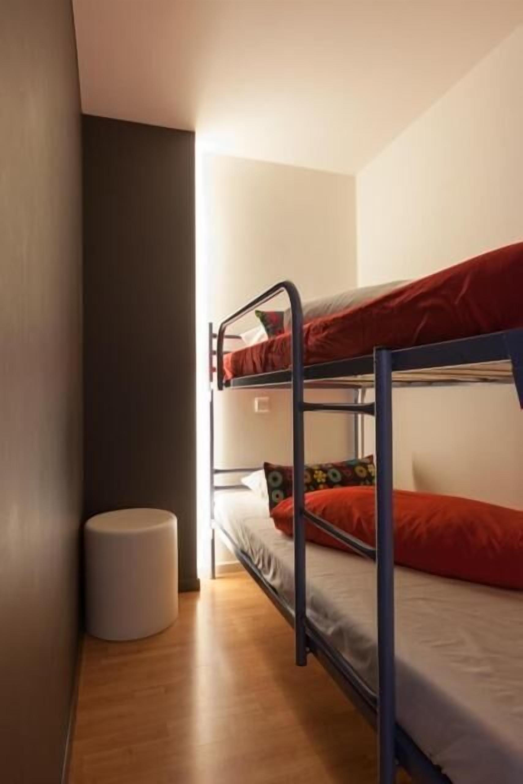A bunk bed room with a small round stool and a light source in the corner.