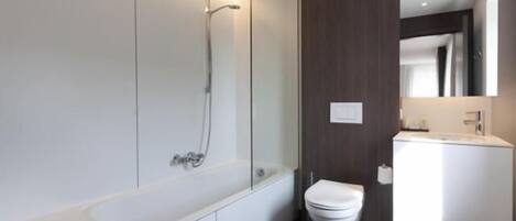 A modern bathroom with a glass-enclosed shower, a white toilet, and a large mirror above the sink.