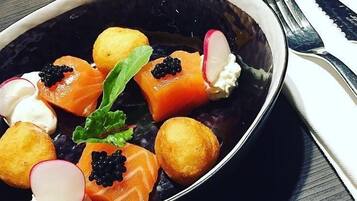 Een schaal eten met zalm, caviaar, radijs en garnering op een donker bord.