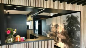 A reception area with a modern design, featuring a wooden panel wall, a large framed historical photograph, and a vase with flowers on the counter. - Hotel La Passerelle (Durbuy)