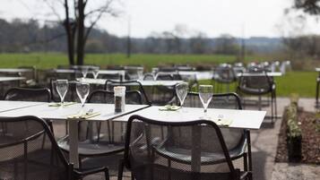 An outdoor dining area with tables and chairs, each set with a wine glass and a salt shaker.