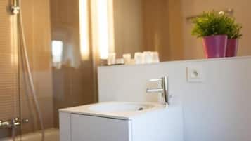 A modern bathroom with a white sink, a glass shower enclosure, and a potted plant on the wall.