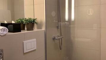 Een moderne badkamer met een douchecabine van glas, een wit toilet, een wastafel met donker aanrechtblad en een spiegel boven de wastafel.