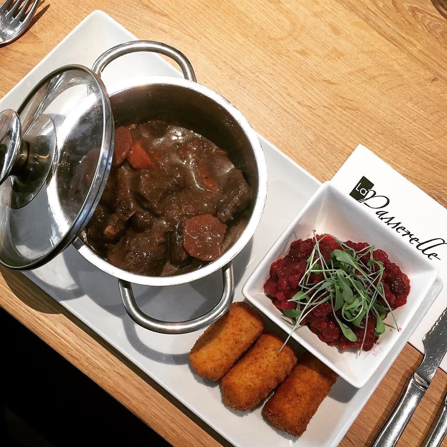 A meal consisting of a stew with meat and vegetables, a bowl of red fruit compote with greens, and two breaded items on a white plate.