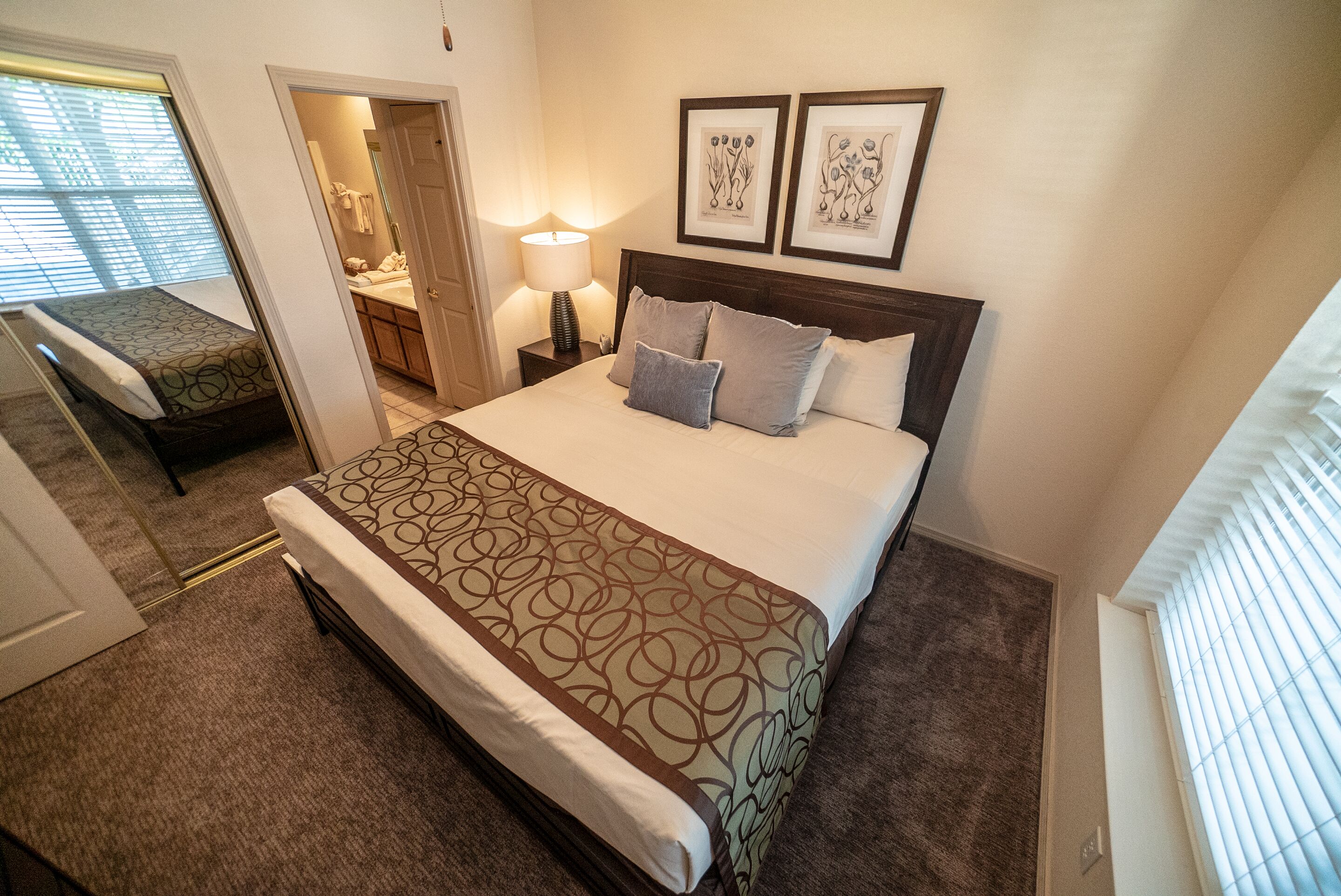 Habitación de hotel con una cama grande, una mesita de noche con lámpara, una pequeña zona de estar con un sillón y cuadros en la pared.