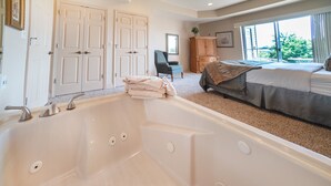 Ein Schlafzimmer mit einer großen Badewanne, einem Bett, einem Schreibtisch und Blick ins Freie.