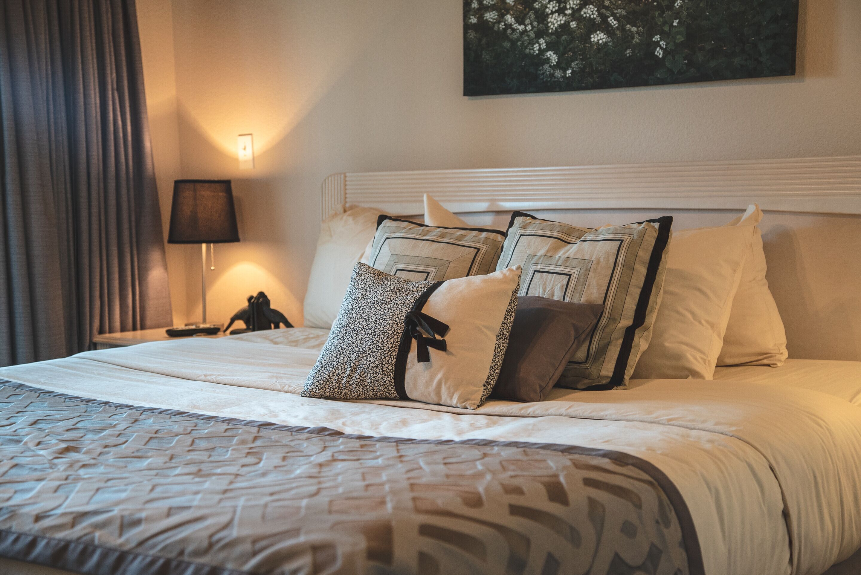 A neatly made bed with patterned bedding and multiple pillows, a bedside lamp, and a wall-mounted artwork.