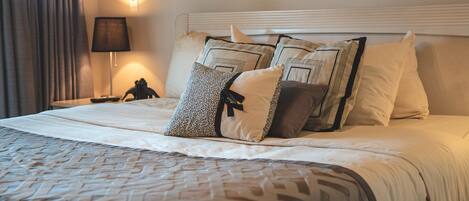 A neatly made bed with patterned bedding and multiple pillows, a bedside lamp, and a wall-mounted artwork.