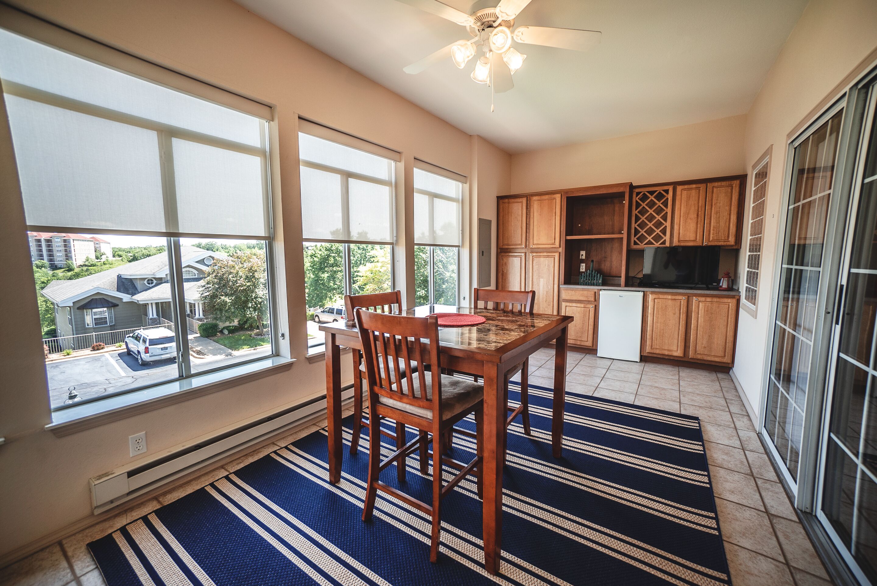 A spacious kitchen with large windows, wooden cabinets, and a dining area with a striped rug.