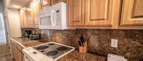 Una cocina con armarios de madera, un microondas blanco, estufa, encimeras de granito y un juego de cuchillos.