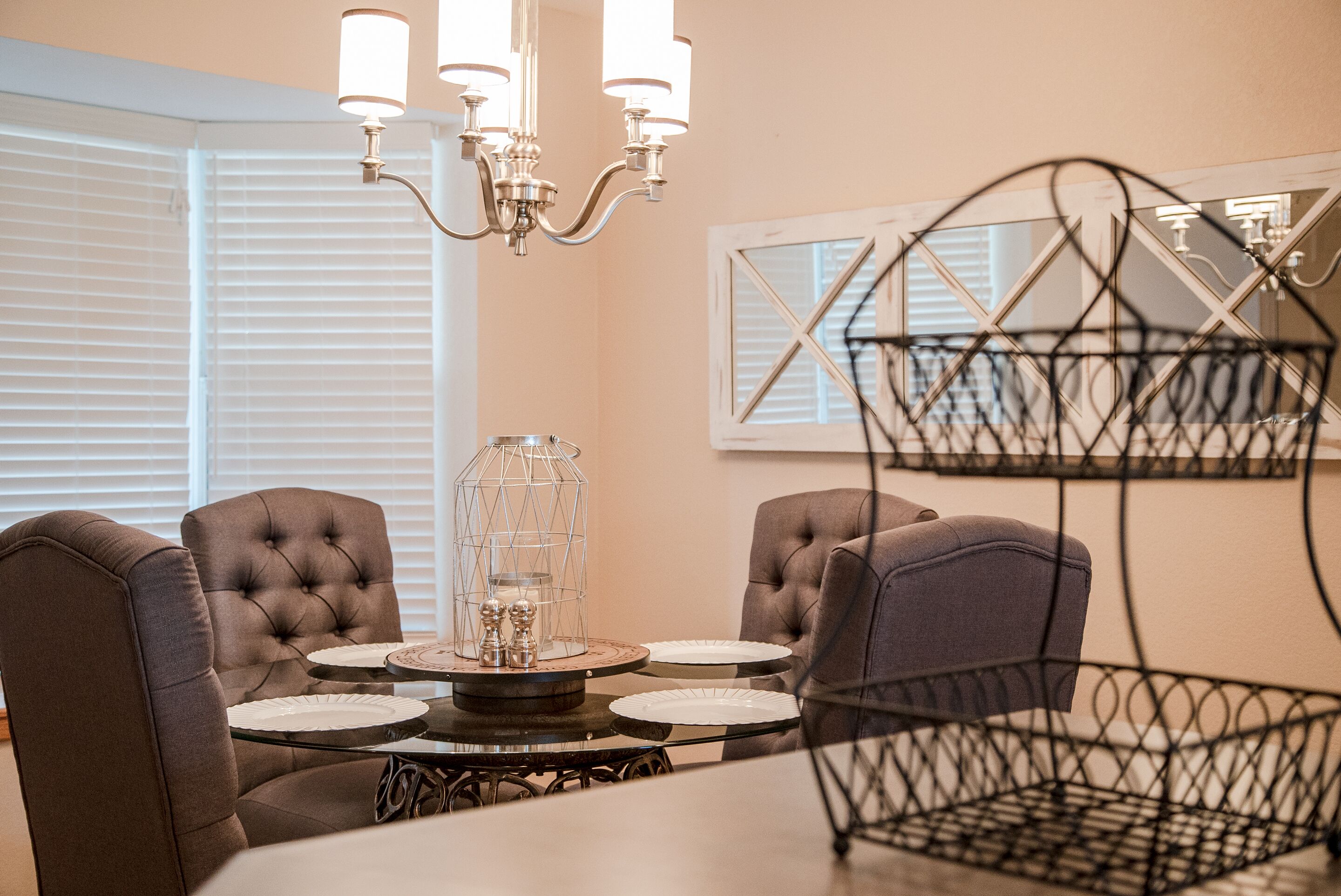 A dining area with a round table, four upholstered chairs, a chandelier, and a decorative glass lantern.