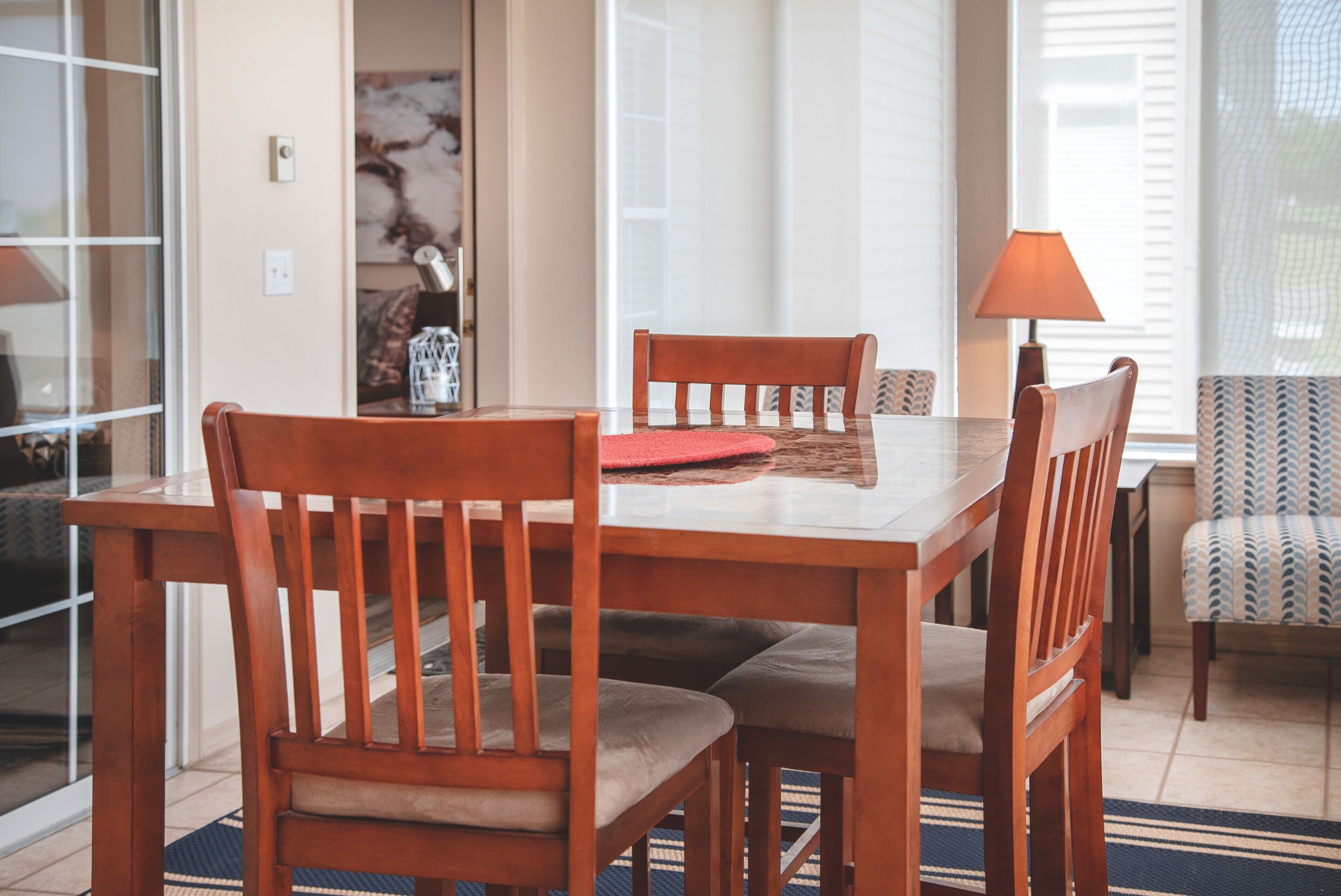 A dining area with a wooden table and chairs, a red placemat, and a lamp.