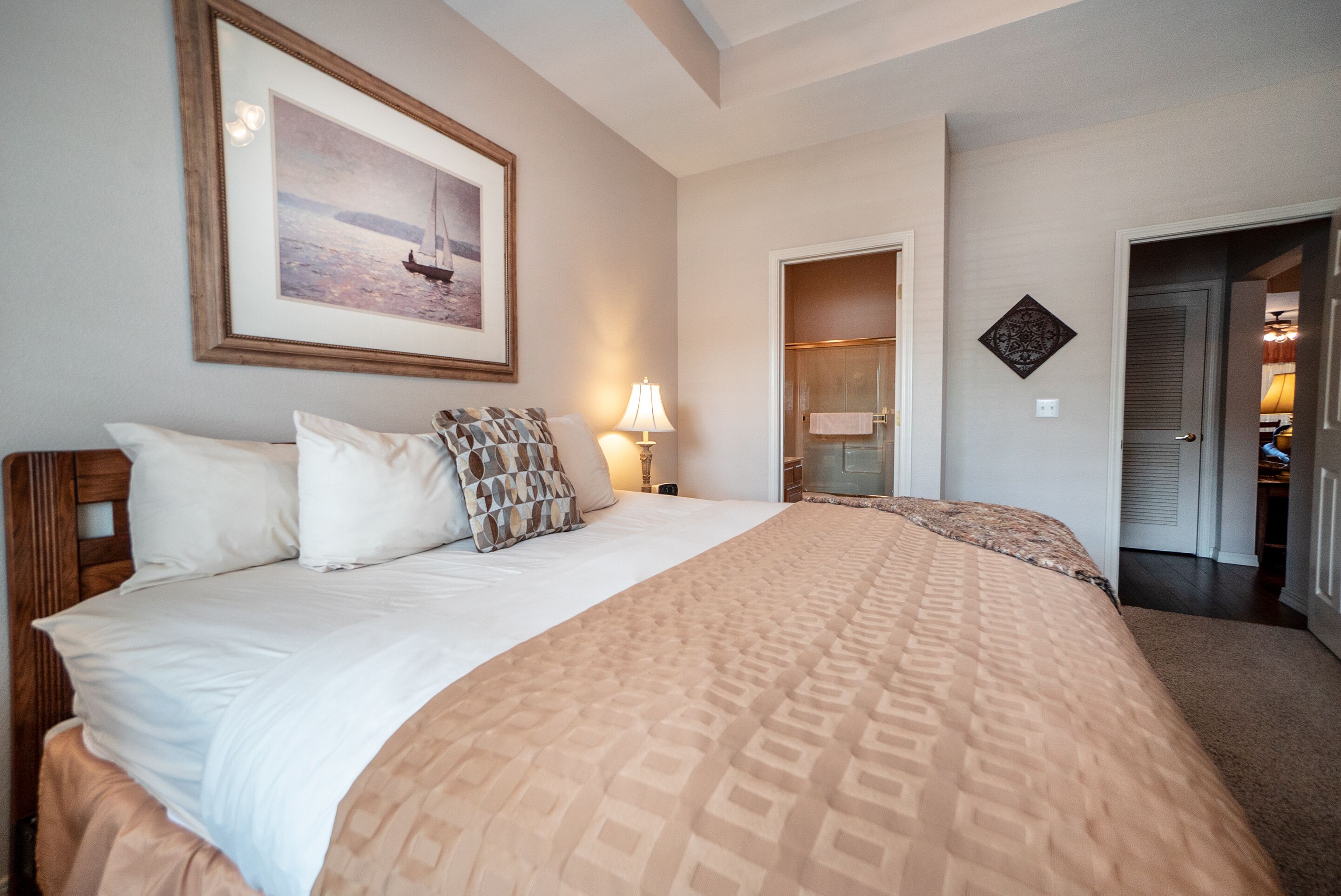 A hotel room with a large bed, a framed picture on the wall, a bathroom visible through an open door, and a small decorative item on the wall.