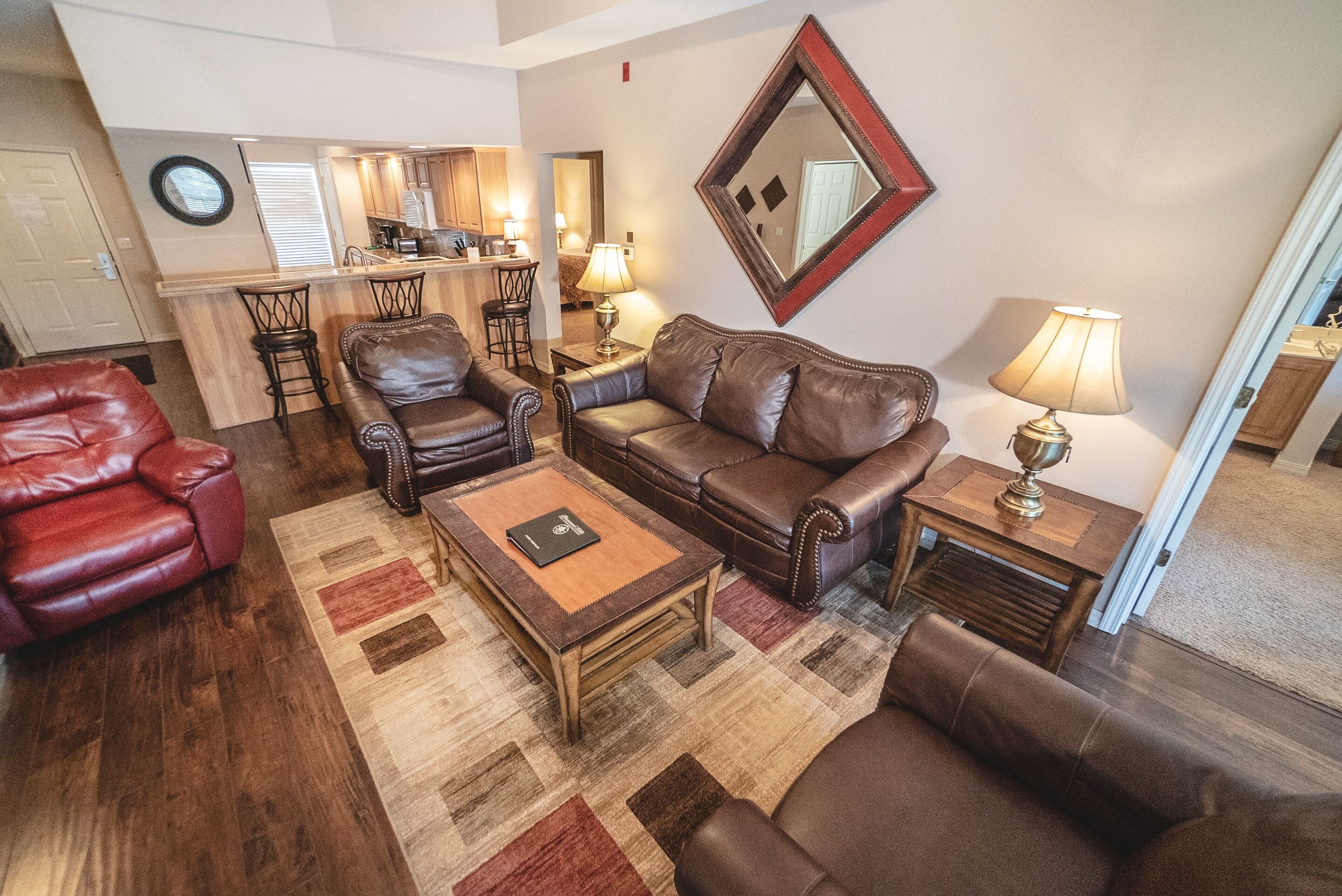 A living room with leather sofas, a coffee table, and a kitchen area in the background.